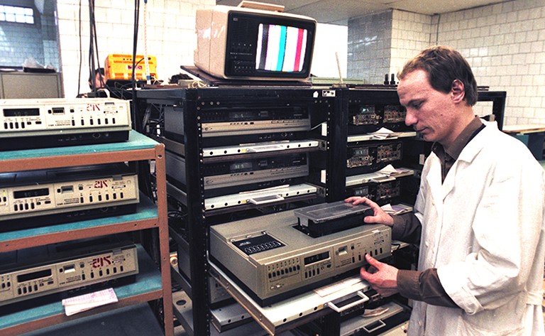 На фото: контролер ОТК А.М. Медников наблюдает за электропрогоном бытовых кассетных видеомагнитофонов "Электроника ВМ-12". Ленинград, 1986 год