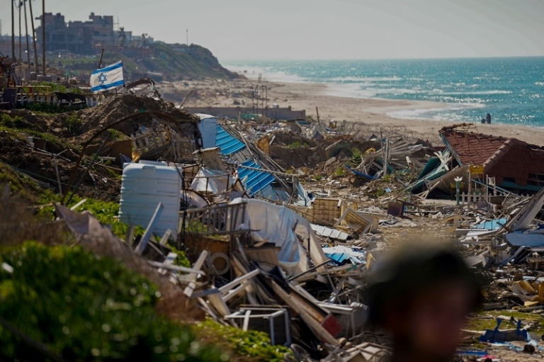 На фото: израильский флаг развевается над разрушенными зданиями на берегу Средиземного моря в секторе Газа.