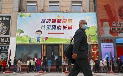 На фото: мужчина в маске для лица на фоне выстраивающихся в очередь за вакциной против COVID-19 и таблички с лозунгом «Своевременная вакцинация, чтобы вместе построить Великую стену иммунитета» в Пекине