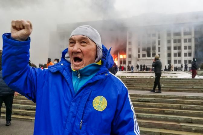 На фото: протестующий возле горящего здания акимата в Алма-Ате. Участники протеста против роста цен на топливо ворвались в здание акимата и пожодгли его.