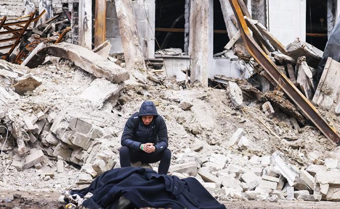 На фото: молодой человек оплакивает погибшего родственника у здания драматического театра Мариуполя, разрушенного в результате обстрелов.