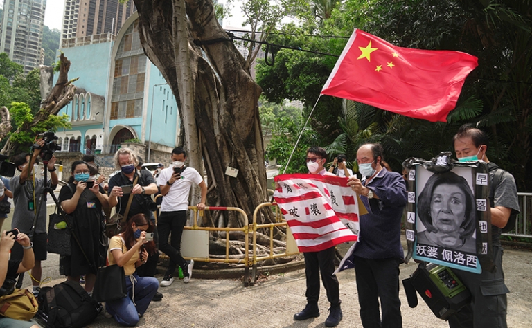 На фото: люди держат флаг США и фото Нэнси Пелоси во время акции протеста. Спикер Палаты представителей США стала самым высокопоставленным американским чиновником, посетившим остров за 25 лет