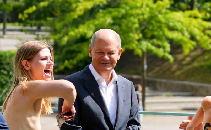 На фото: две активистки, стоящие рядом с канцлером Германии Олафом Шольцем (в центре), протестуют против газового эмбарго во время акции «открытых дверей» в канцелярии в Берлине, Германия