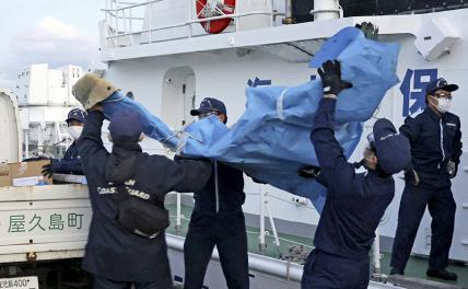 На фото: члены японской береговой охраны несут обломки, которые, предположительно, остались от разбившегося американского военного самолета Osprey, в порту Якусима, префектура Кагосима, южная Япония, 4 декабря 2023 года