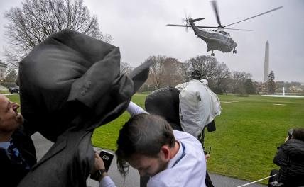 На фото: операторы закрываются от ветра и дождя, в то время, как самолет Marine One с президентом Джо Байденом взлетает с Южной лужайки Белого дома в Вашингтоне.