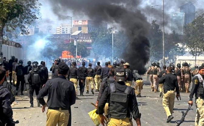 На фото: полицейские преследуют мусульман-шиитов, перекрывших дорогу и поджигающих шины во время протеста против убийства верховного лидера Ирана аятоллы Али Хаменеи, в Карачи, Пакистан.