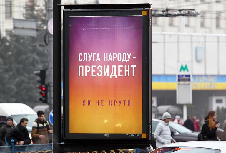 На фото: люди проходят мимо плаката с надписью «Слуга народа - президент!» в Киеве, Украина, 31 января 2019 года. «Слуга народа» - телевизионный сериал с украинским актером и кандидатом на президентских выборах Владимиром Зеленским в главной роли. Сериал рассказывает историю Василия Голобородько (актер Владимир Зеленский), тридцатилетнего учителя истории средней школы, который побеждает на выборах в президенты Украины после вирусного видео, в котором он выступает против коррупции правительства в Украине