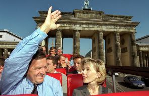 На фото: канцлер Германии Герхард Шредер (слева) машет рукой с верхней палубы открытого экскурсионного автобуса у Бранденбургских ворот во время поездки по Берлину, Германия, рядом со своей женой Дорис Шредер-Кепф (справа) 25 августа 1999 года