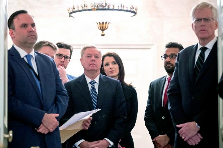 На фото: директор по социальным сетям Белого дома Дэн Скавино (слева), сенатор Линдси Грэм (RS.C.) (в центре слева), старший директор Совета национальной безопасности по борьбе с терроризмом Кашьяп &laquo;Каш&raquo; Прамод Патель (второй справа) и старший директор Совета национальной безопасности по борьбе с терроризмом и сетями угроз Крис Миллер (справа) наблюдают за выступлением президента Дональда Трампа в Дипломатическом зале Белого дома в Вашингтоне, 2019 год.